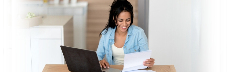 Happy woman reviewing energy bills at home after implementing energy-efficient landscaping.