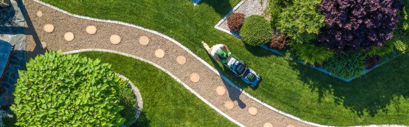 Gardener with Grass Mower Trimming Backyard Lawn